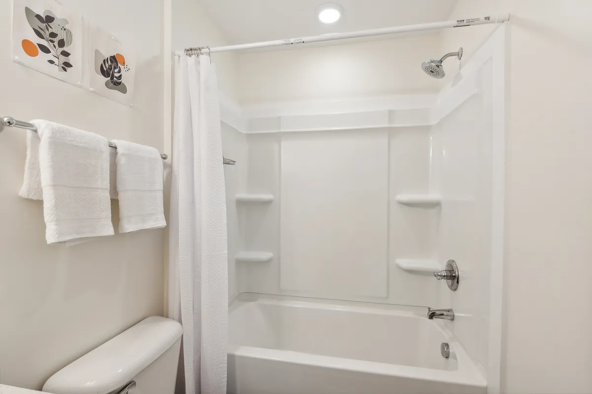 A stylish bathroom featuring a bathtub with a showerhead, neatly hung towels, and tasteful wall art. The atmosphere is serene and inviting, ideal for both soothing baths and quick showers.