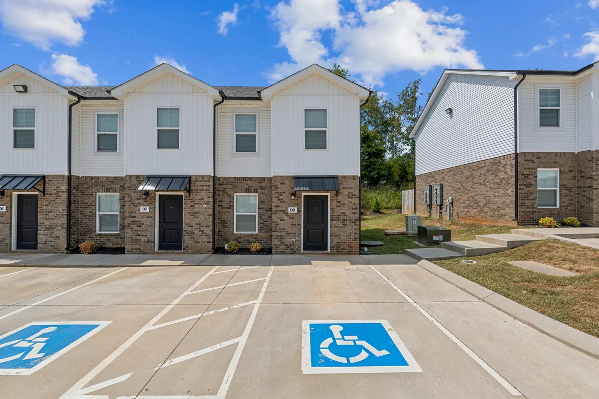 This exterior image showcases the welcoming townhouse architecture, clearly displaying the building’s approachable facade, well-maintained landscaping, and convenient parking area directly adjacent to the units. The scene suggests a comfortable, community-oriented environment ideal for business travelers seeking ease of arrival and departure.